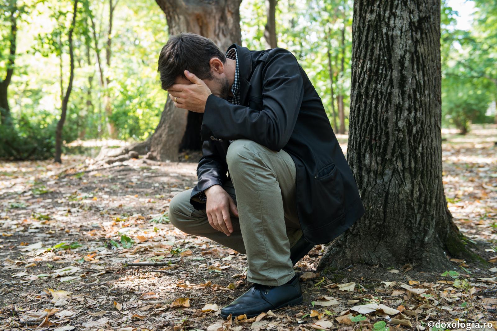 bărbat demoralizat în pădure ținând mâna la cap