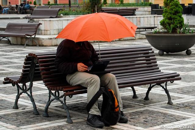 bărbat stând pe bancă cu umbrelă și laptop