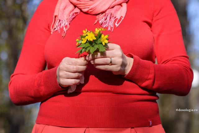 femeie în bluză roșie cu un buchet mic de flori galbene în mână