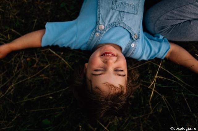 copil întins pe iarbă zâmbind