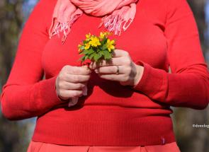femeie în bluză roșie cu un buchet mic de flori galbene în mână