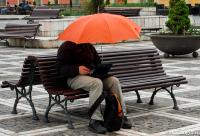 bărbat stând pe bancă cu umbrelă și laptop