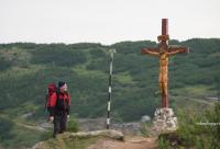 bărbat privind o cruce de lemn pe vârful muntelui